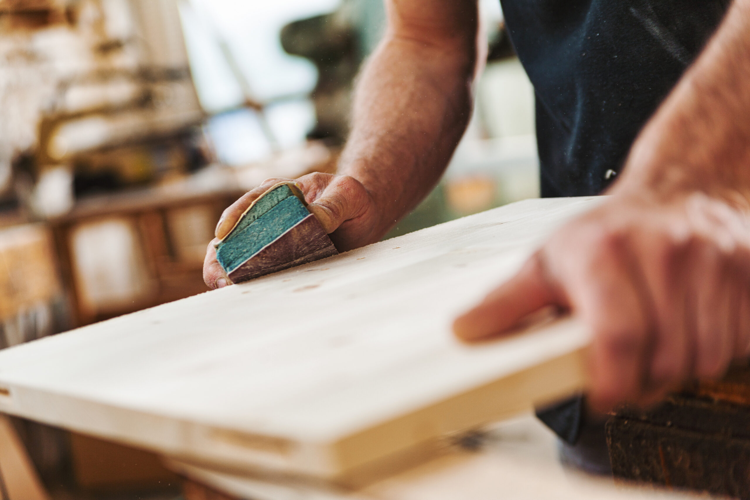 Carpenter sanding wood using sandpaper in workshop